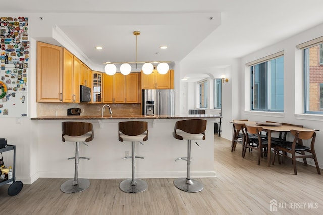 kitchen featuring glass insert cabinets, a sink, black microwave, stainless steel fridge, and a peninsula