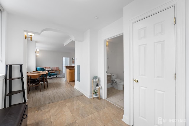 hall featuring arched walkways, light tile patterned flooring, and baseboards