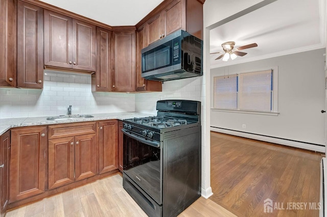 kitchen with light stone counters, a baseboard radiator, stainless steel microwave, black gas stove, and a sink