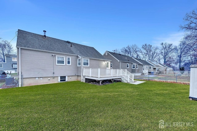 rear view of house with roof with shingles, a lawn, a wooden deck, and fence