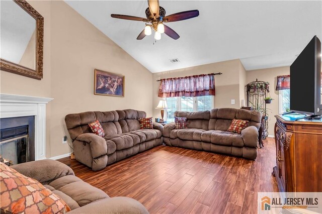 living area featuring visible vents, a glass covered fireplace, lofted ceiling, ceiling fan, and wood finished floors