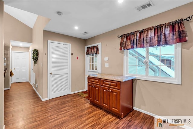 kitchen with brown cabinetry, visible vents, baseboards, and wood finished floors