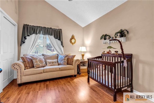 bedroom with a nursery area, high vaulted ceiling, and wood finished floors