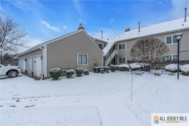 snow covered property featuring central AC unit and a garage