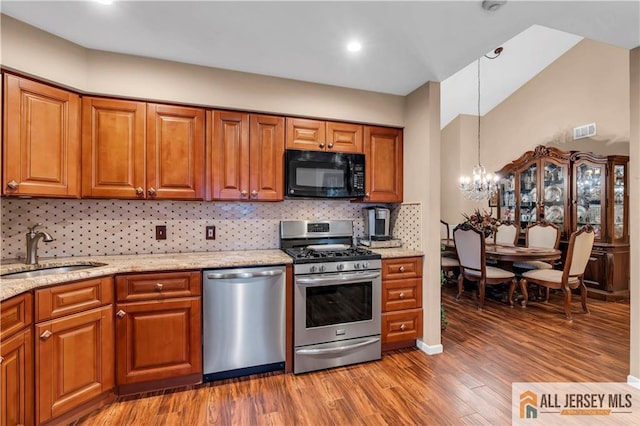 kitchen with pendant lighting, appliances with stainless steel finishes, sink, backsplash, and a notable chandelier