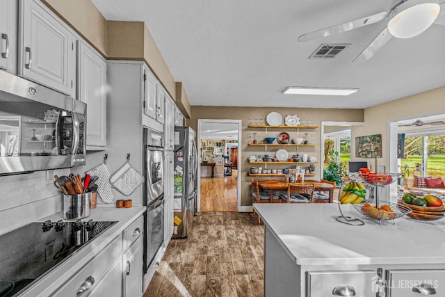 kitchen with dark wood-type flooring, ceiling fan, appliances with stainless steel finishes, white cabinetry, and decorative backsplash