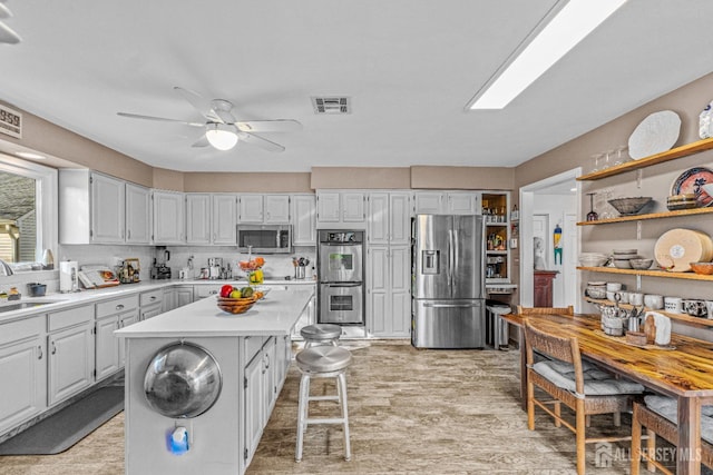 kitchen with sink, a kitchen island, ceiling fan, stainless steel appliances, and white cabinets