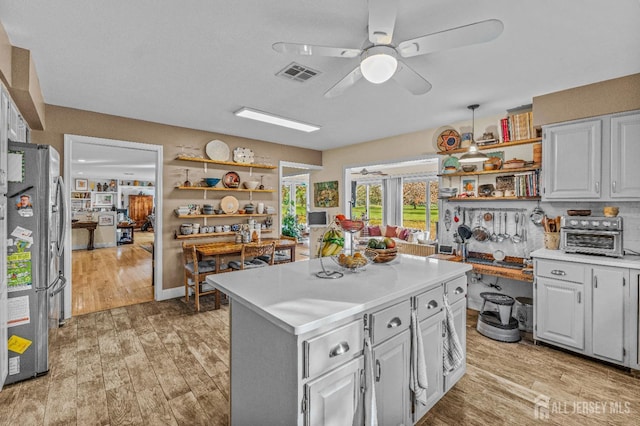 kitchen featuring stainless steel refrigerator, ceiling fan, white cabinetry, a center island, and light wood-type flooring