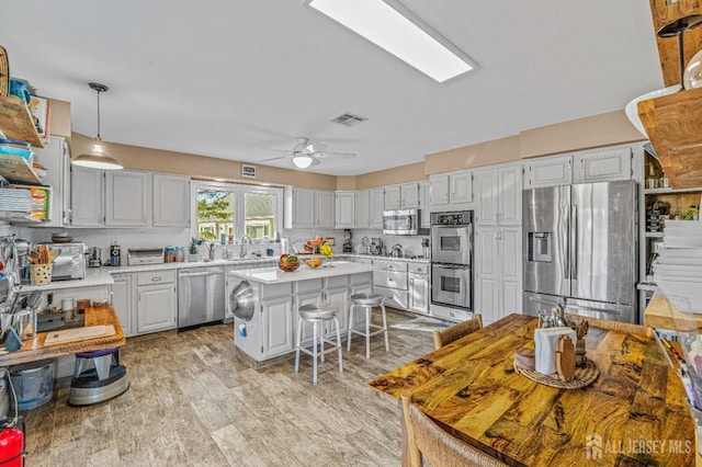 kitchen with sink, stainless steel appliances, white cabinets, a kitchen island, and decorative light fixtures