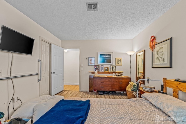 bedroom with a textured ceiling, light wood-type flooring, and a closet