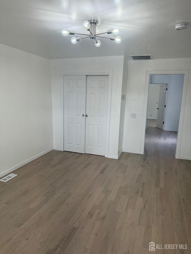 unfurnished bedroom featuring wood-type flooring, a notable chandelier, and a closet