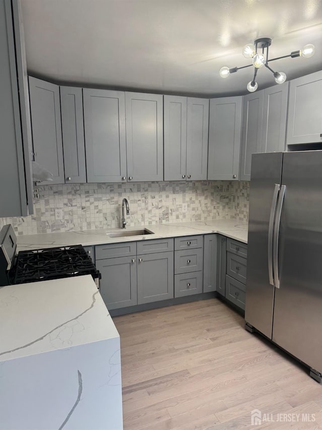 kitchen with sink, appliances with stainless steel finishes, gray cabinets, light hardwood / wood-style floors, and backsplash