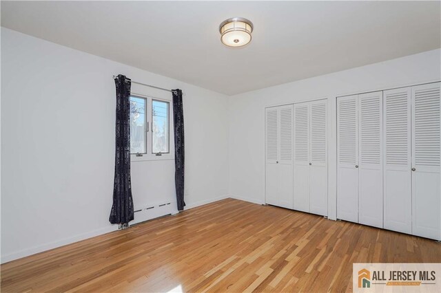 unfurnished bedroom featuring hardwood / wood-style flooring, a baseboard heating unit, and two closets