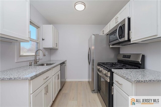 kitchen with sink, light stone counters, light hardwood / wood-style flooring, stainless steel appliances, and white cabinets