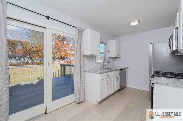 kitchen featuring appliances with stainless steel finishes, sink, white cabinets, light stone counters, and light hardwood / wood-style floors