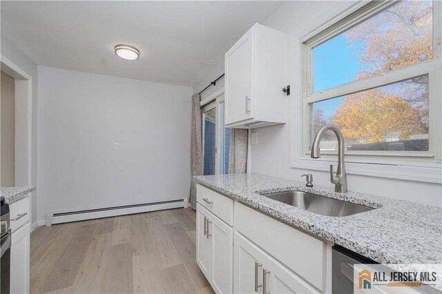 kitchen featuring white cabinetry, sink, light stone counters, baseboard heating, and light hardwood / wood-style floors