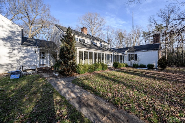view of front of home featuring a sunroom, a front lawn, and a chimney