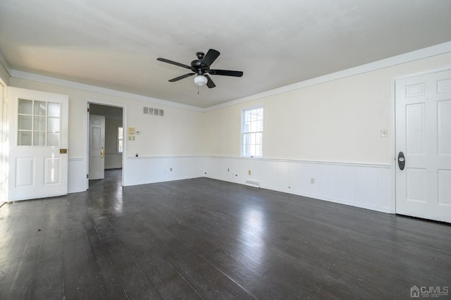 unfurnished living room with ornamental molding, dark wood finished floors, ceiling fan, and a wainscoted wall