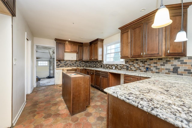 kitchen with light stone countertops, hanging light fixtures, baseboards, backsplash, and a kitchen island