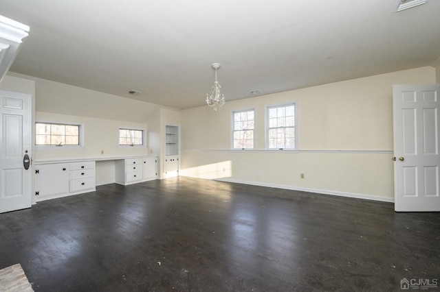 empty room featuring dark wood-style flooring, a notable chandelier, plenty of natural light, and built in study area