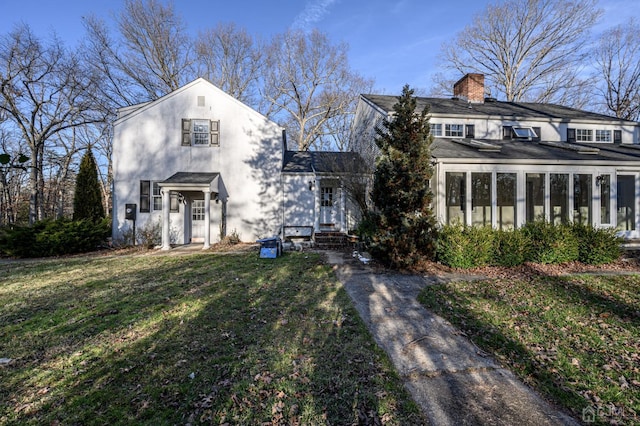 view of front facade with a sunroom, a chimney, roof with shingles, and a front lawn