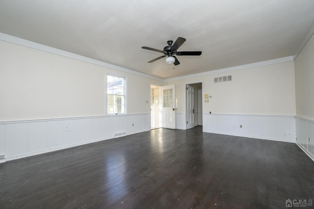 unfurnished room featuring crown molding, a wainscoted wall, a ceiling fan, and dark wood finished floors