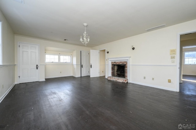 unfurnished living room with an inviting chandelier, baseboards, a brick fireplace, and wood finished floors