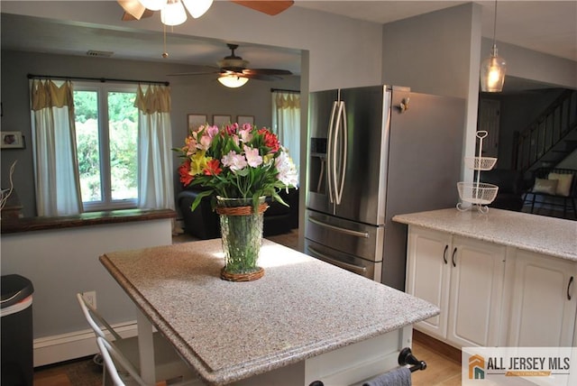 kitchen featuring light stone countertops, white cabinets, stainless steel fridge, baseboard heating, and a center island