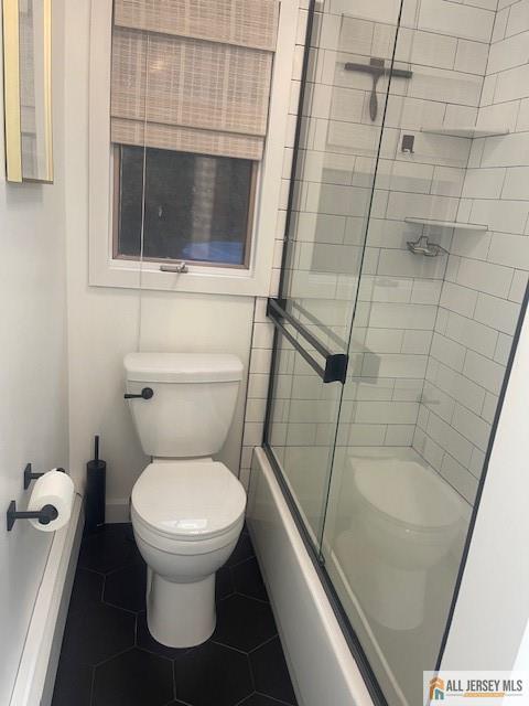 full bath with tile patterned flooring, combined bath / shower with glass door, and toilet