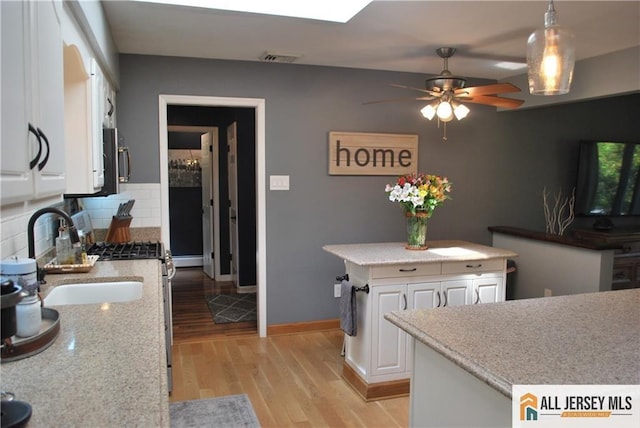 kitchen with a sink, stainless steel appliances, light wood-style floors, white cabinetry, and backsplash