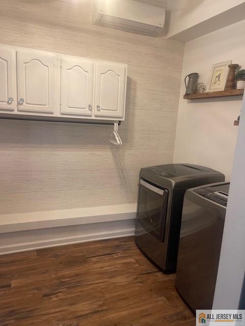 clothes washing area featuring a wall mounted AC, dark wood-style floors, cabinet space, and washing machine and clothes dryer