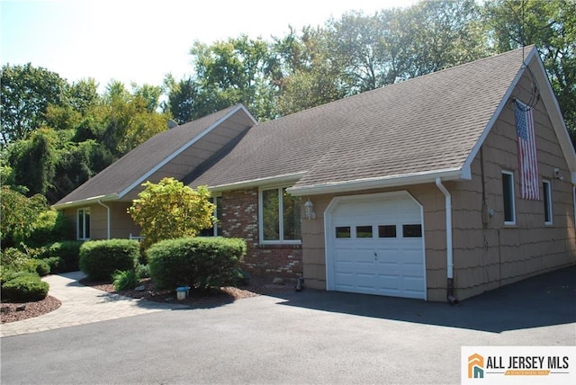 view of front facade featuring brick siding, driveway, an attached garage, and roof with shingles