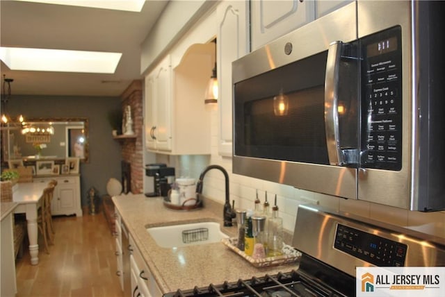 kitchen with a sink, decorative backsplash, white cabinets, appliances with stainless steel finishes, and light wood-type flooring