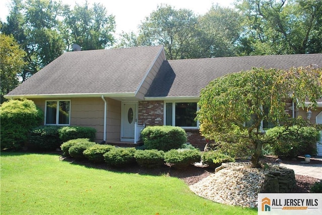 view of front of property with brick siding, a front lawn, and a shingled roof