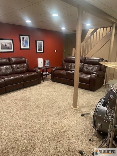 living room with a paneled ceiling, carpet, and stairs