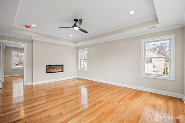 unfurnished living room with a tray ceiling, visible vents, and ornamental molding