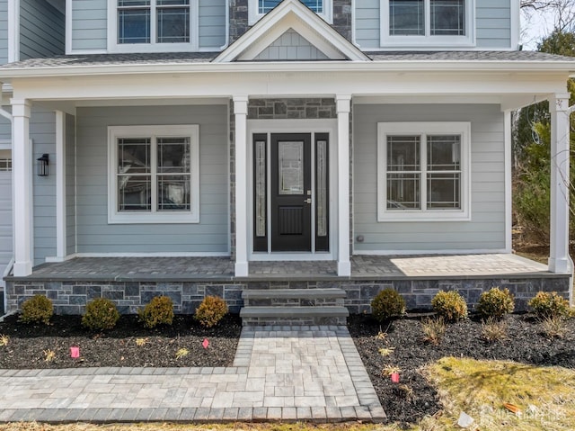entrance to property featuring roof with shingles and a porch