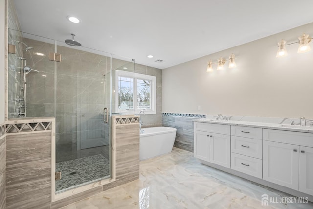 full bath featuring a stall shower, a freestanding bath, tile walls, and a sink