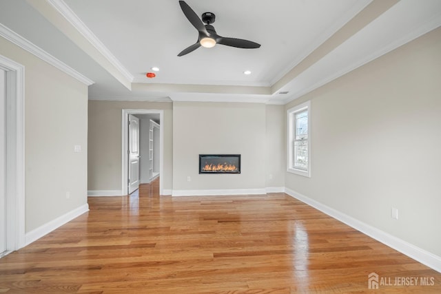 unfurnished living room with light wood finished floors, a glass covered fireplace, a raised ceiling, and baseboards