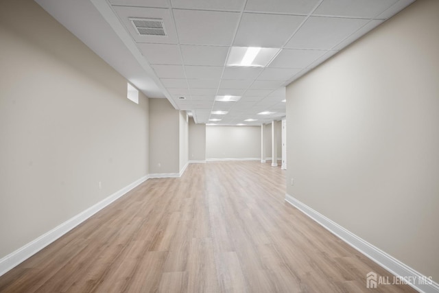 finished basement featuring a paneled ceiling, visible vents, baseboards, and light wood-style floors