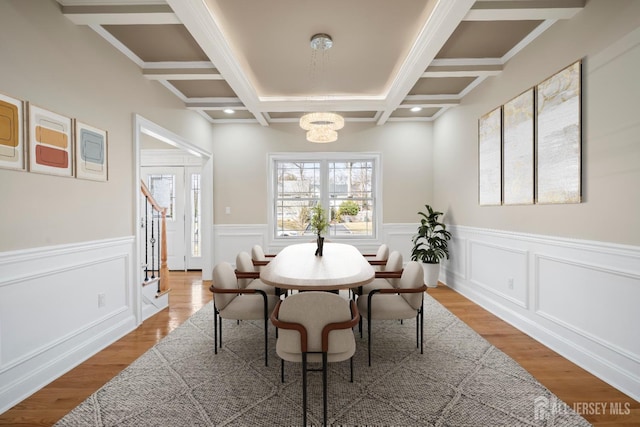 dining area featuring light wood-style flooring, a wainscoted wall, beam ceiling, a notable chandelier, and coffered ceiling