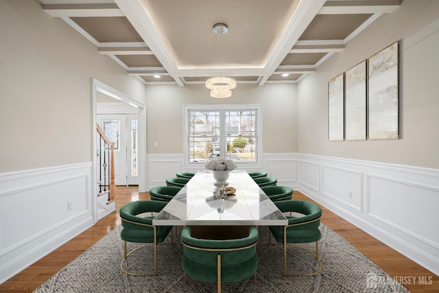 dining area featuring a wainscoted wall, beam ceiling, an inviting chandelier, wood finished floors, and coffered ceiling