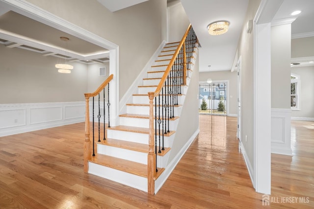 stairs featuring a wainscoted wall, visible vents, a chandelier, wood finished floors, and a decorative wall