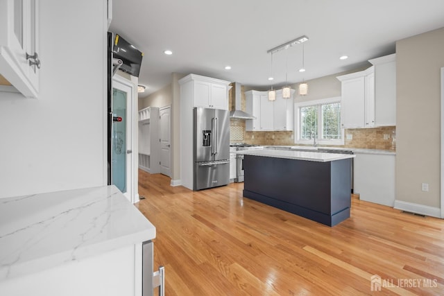 kitchen featuring stainless steel appliances, decorative backsplash, white cabinetry, wall chimney exhaust hood, and light wood-type flooring