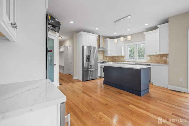 kitchen with stainless steel appliances, backsplash, white cabinetry, and wall chimney range hood