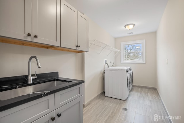 clothes washing area featuring cabinet space, washing machine and dryer, baseboards, and a sink