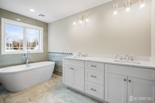 bathroom with a freestanding bath, tile walls, visible vents, and a sink