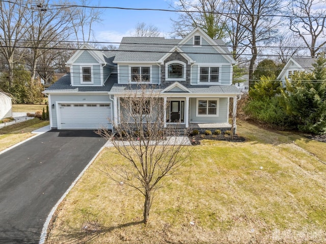 shingle-style home featuring aphalt driveway, a garage, covered porch, and a front lawn