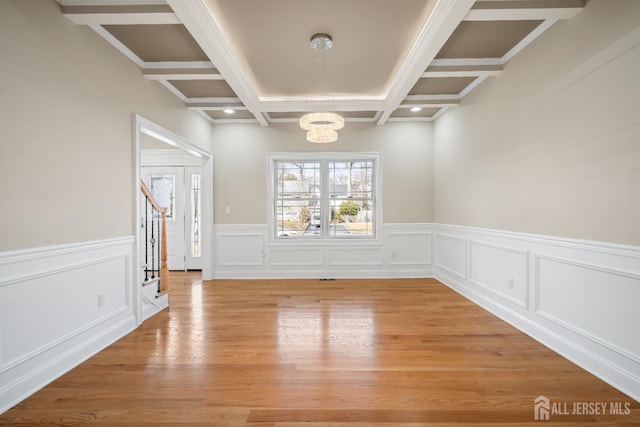 empty room featuring beamed ceiling, coffered ceiling, an inviting chandelier, and light wood-style flooring