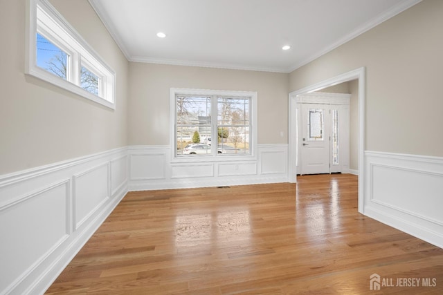 unfurnished dining area with a decorative wall, ornamental molding, a wainscoted wall, and light wood-type flooring